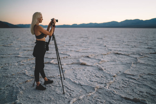 Young female photographer shoot sunset in Death Valley using digital camera and tripod, tourist woman making pictures of wild landscape of Badwater basin in evening dusk having journalistic expedition - Foto, afbeelding