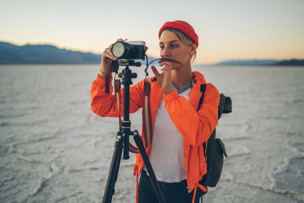 Pensive female journalist concentrated on making setting for shooting view of landscape in expedition, skilled photographer taking pictures of natural landscape in Badwater national park using tripo - Photo, image