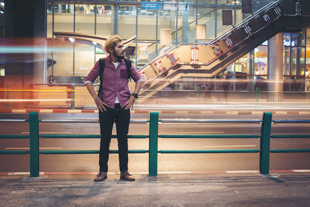 Hipster bearded man backpacker standing with car motion background while traveling at night. - Foto, afbeelding