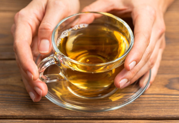 Female hands holding aromatic fresh tea on wooden table - Photo, image