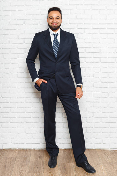 Portrait of young fashionable man in suit on brick wall background - 写真・画像