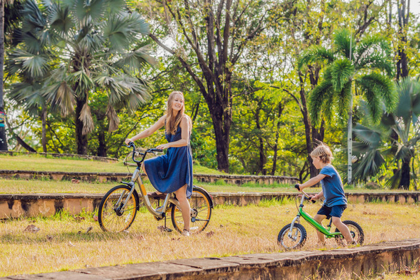 Mother and son riding bikes outdoors and smiling - Фото, изображение