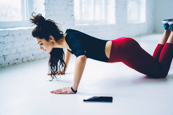 Determined woman doing push ups exercises for training chest and arms muscles in white interior gym,slim strong girl planking from knees having hard workout for keeping athletic body shape - Photo, Image