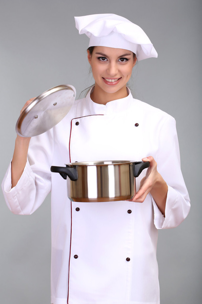 Portrait of young woman chef with pan on grey background - Photo, image