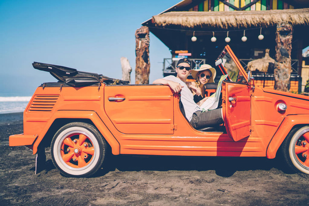 Male and female tourists making car stop on ocean beach enjoying summer vacation together in roadtrip,hipster couple renting automobile for exploring Bali during honeymoon recreating on vacations - Photo, Image