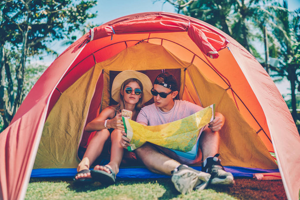 Hipster girl browsing information on smartphone while discussing route with boyfriend sitting in tent,couple in love reading map planning trip camping during journey spending summer vacations together - Zdjęcie, obraz