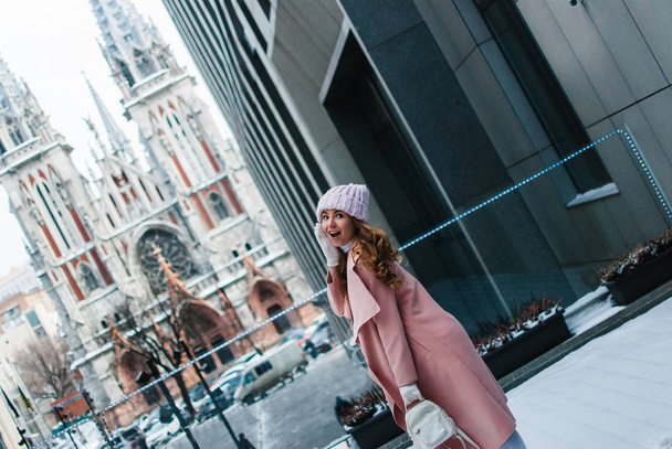 Winter cutie. Beautiful young woman in pink coat looking at camera with smile while standing outdoors. - Photo, Image