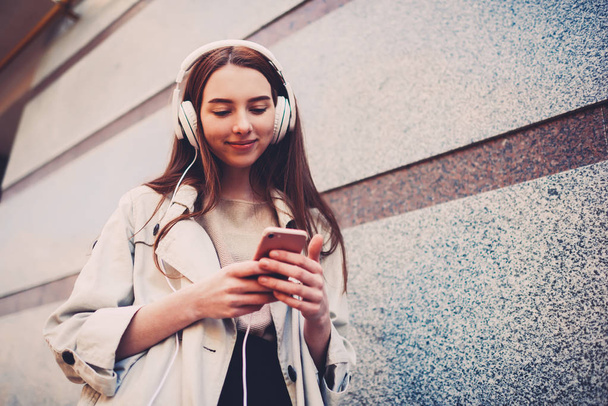 Young trendy dressed female student watching videos browsing on websites using smartphone and 4G internet connection outdoors, hipster girl using application for listening to music from playlist - Foto, immagini