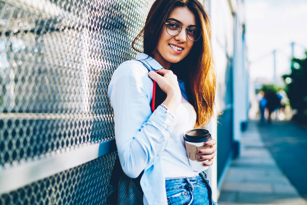 Half length portrait of cheerful brunette student in stylish optical eyeglasses smiling at camera while spending recreation time on walk on street.Positive hipster girl standing near copy space area - Valokuva, kuva