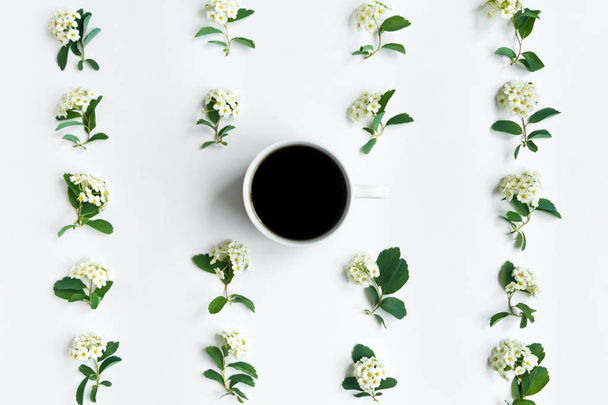 Cup of coffee and flowering Spirea arguta (brides plant) branches on white table. Flat lay, top view - Photo, Image