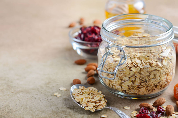 Ingredients for homemade oatmeal granola. Oat flakes, honey, almond nuts, dried cranberries and apricots. Healthy breakfast concept. - Photo, Image