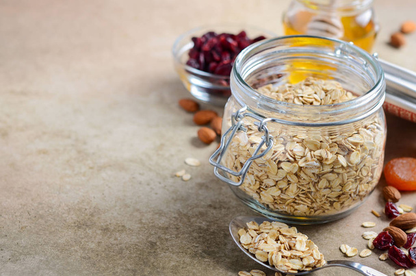 Ingredients for homemade oatmeal granola. Oat flakes, honey, almond nuts, dried cranberries and apricots. Healthy breakfast concept. - Photo, Image