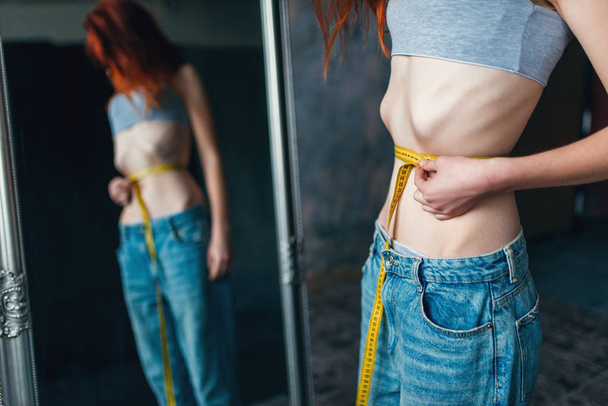 mulher magra que mede a cintura contra o espelho, perda de peso, anorexia
 - Foto, Imagem
