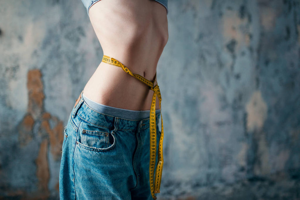 dünne Frau in Jeans, die ihre Taille misst, Gewichtsverlust, Magersucht-Konzept  - Foto, Bild