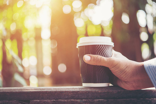 Hombre mano sosteniendo la taza de papel de café sobre fondo natural de la mañana
. - Foto, Imagen