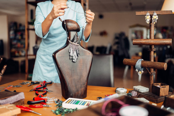 vrouw probeert op handgemaakte ketting op houten mannequin, handwerk - Foto, afbeelding