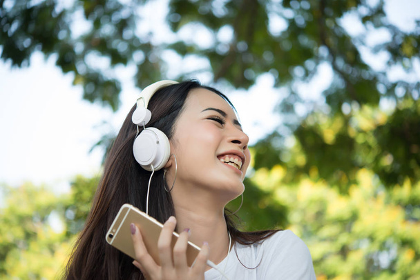 Portrait of a smiling girl with headphones listening to music while relaxing in nature park outdoors. - Foto, imagen