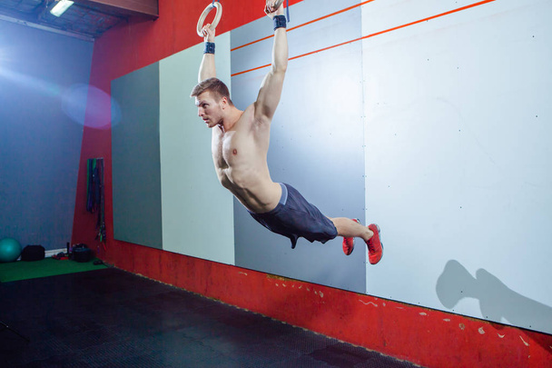 Muscle-up exercise young man doing intense cross fit workout at the gym on gymnastic rings. - Фото, изображение