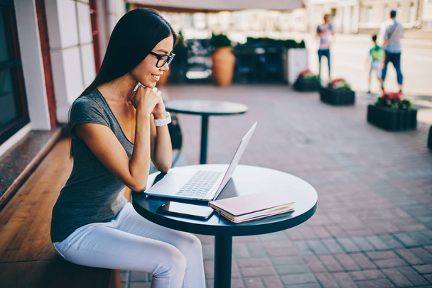 Young hipster girl enjoying watching video on laptop spending time on cafe terrace with laptop,positive female freelancer satisfied with earning money online reading notification during banking - Foto, Bild