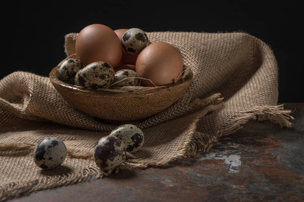 Kip en kwartel eieren in kom op rustieke houten achtergrond - Foto, afbeelding
