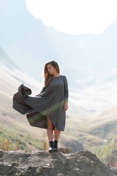 A beautiful girl in a flying dress is standing by a cliff in the mountains - Фото, зображення