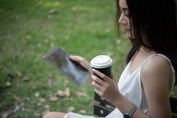 Молодая красивая женщина держит одноразовый кофе чашку в то время как текстовые сообщения через смартфон на природе
. - Фото, изображение
