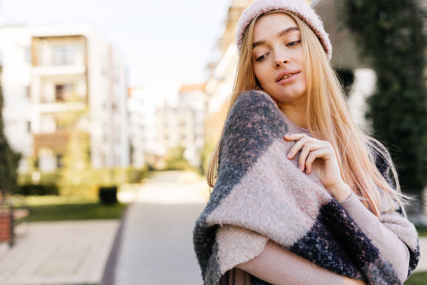 cute young girl blond model in hat, on shoulders warm scarf, walking outdoors - Fotó, kép