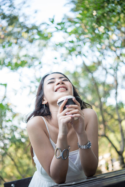 Jeune femme tenant tasse de café jetable tout en étant assis profiter de la nature en plein air
. - Photo, image