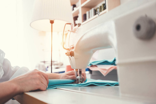 Sewing machine and female hands of dressmakers close-up. Young businesswoman working in clothes design bureau. Small business. Flare effect - Zdjęcie, obraz