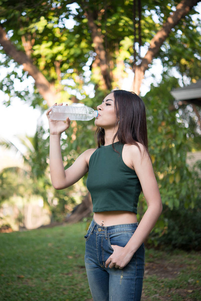 Молода красива жінка розслабляється на відкритому повітрі п'є воду в парку
. - Фото, зображення