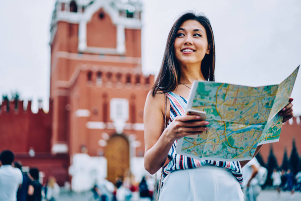 Attractive asian girl standing on red square in moscow enjoying sightseeing tour with map, cheerful female tourist getting to location near Kremlin on background planning next route in Moscow - Zdjęcie, obraz