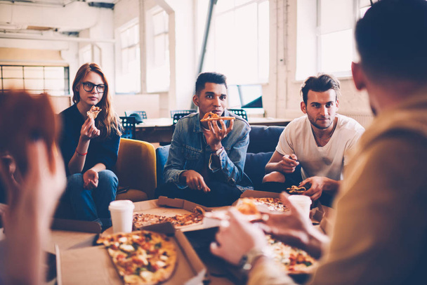 Multiracial group of international student talking to each other and making friends during pizza party, hungry male and female employees having lunch break together eating in coworking space - Foto, Bild