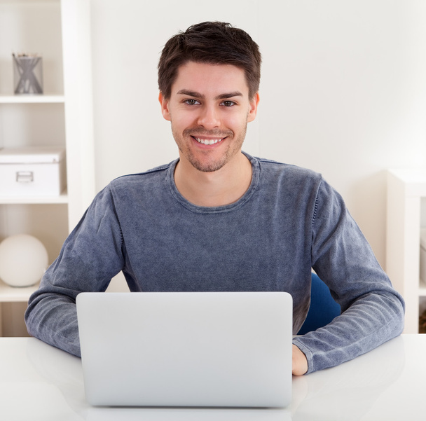χαμογελαστός νεαρός χρησιμοποιώντας ένα φορητό υπολογιστή - Φωτογραφία, εικόνα