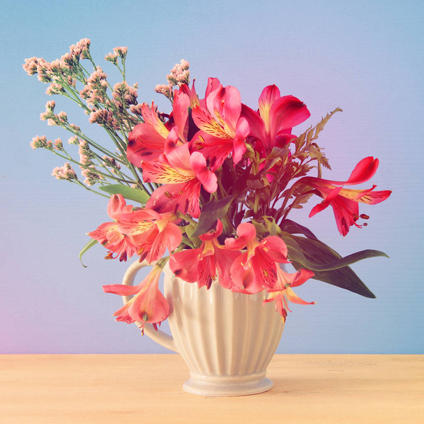 summer bouquet of red flowers in the vase over wooden table and blue background. - 写真・画像