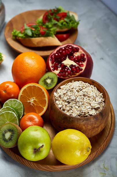 Bowl with oatmeal flakes served with fruits on wooden tray over rustic background, flat lay, selective focus - 写真・画像