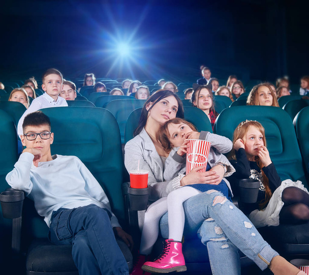 Senior sister is watching movie in the cinema hall with junior children . - Фото, зображення