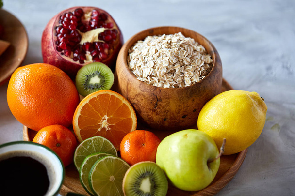 Bowl with oatmeal flakes served with fruits on wooden tray over rustic background, flat lay, selective focus - Фото, зображення