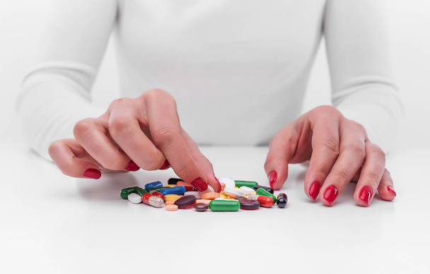 Woman chooses medicine from a handful of different color tablets. - Фото, изображение