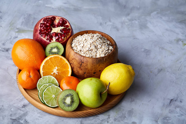 Bowl with oatmeal flakes served with fruits on wooden tray over rustic background, flat lay, selective focus - Foto, Imagem