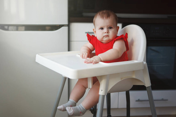 baby in a red dress is sitting on a child's chair - Φωτογραφία, εικόνα