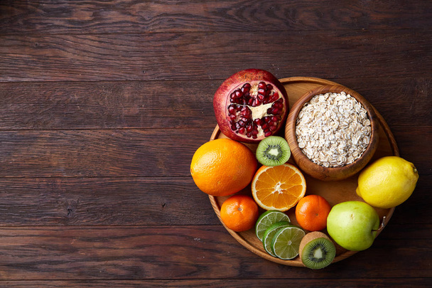 Bowl with oatmeal flakes served with fruits on wooden tray over rustic background, flat lay, selective focus - 写真・画像
