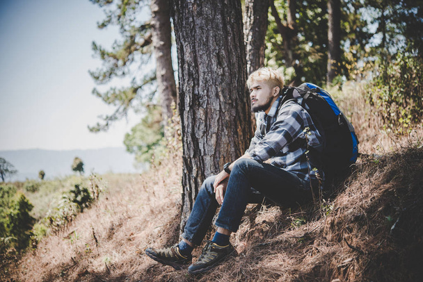 junger müder Wanderer mit Rucksack auf dem Berggipfel sitzend, während er sich nach einem aktiven Spaziergang ausruht. - Foto, Bild