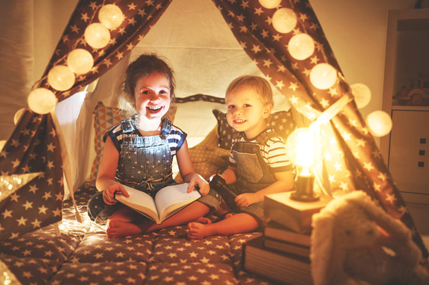 dzieci chłopiec i dziewczynka czytania książki z latarką w namiocie  - Zdjęcie, obraz