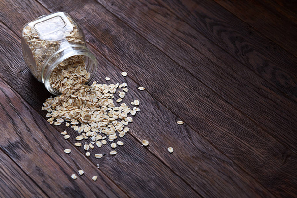 Overturned glass jar and spoon with raw oatmeal on vintage wooden background, close-up, selective focus. - Fotografie, Obrázek