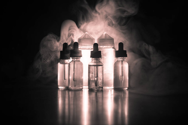 Vape concept. Smoke clouds and vape liquid bottles on dark background. Light effects - Fotoğraf, Görsel