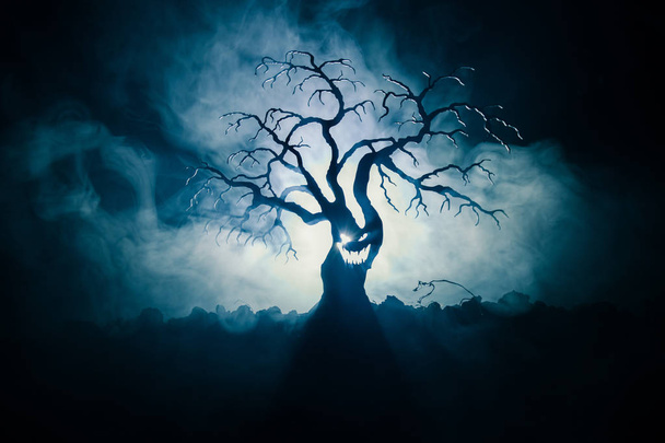 Silhouette eines gruseligen Halloween-Baumes mit Horrorgesicht auf dunklem, nebelfarbenen Hintergrund mit Mond auf der Rückseite. Gruseliger Horrorbaum mit Zombie- und Dämonengesichtern. - Foto, Bild