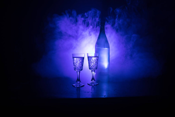 Δύο ποτήρια βότκα με μπουκάλι σε σκοτεινό, ομιχλώδη club στυλ φόντου με λαμπερό παραδεισένιους φώτα (Laser, Stobe). Λέσχη ποτά θέμα διακόσμησης. Κενός χώρος - Φωτογραφία, εικόνα