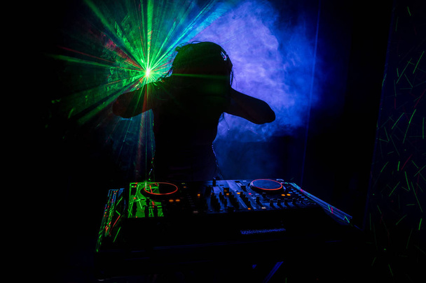 DJ dreht, mischt und kratzt in einem Nachtclub, Hände von DJ zwicken verschiedene Trackregler auf dem DJ-Deck, Blitzlicht und Nebel, oder DJ mischt den Track im Nachtclub auf der Party - Foto, Bild