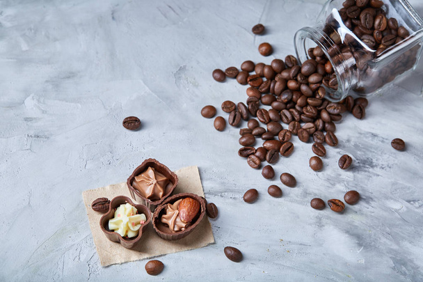 Side view of overturned glass jar with coffee beans and chocolate candies on wooden background, selective focus - Фото, зображення