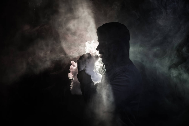 Vaping man holding a mod. A cloud of vapor. Black background. Vaping an electronic cigarette with a lot of smoke. Vape concept - Photo, Image